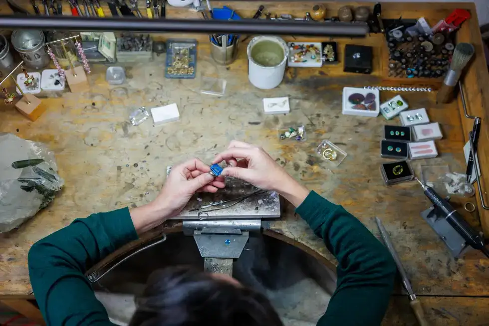 Manon aan het werk aan haar werkbank in het atelier, omringd door edelstenen en gereedschap
